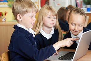 Three children gathered around a laptop, engaged and smiling as they interact with it.