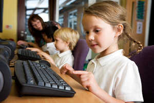 Children using computers in a classroom setting with a woman supervising.