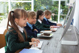 Children working on computers at a wooden table, focused and engaged in their tasks.