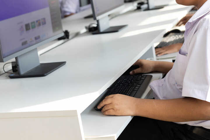 Student typing on a keyboard at a computer workstation.