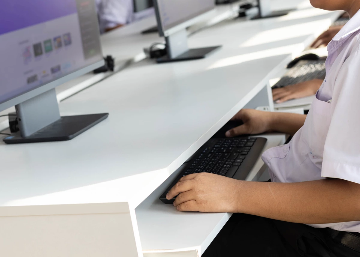 Student using a computer at a desk in a classroom setting.