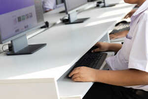 Student typing on a keyboard at a computer workstation.