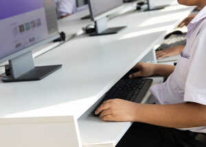 Student using a computer at a desk in a classroom setting.