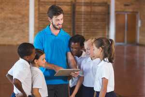 A coach shows a group of four young students something on a tablet.