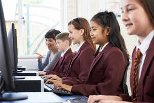 Students in school uniforms working on computers in a classroom setting.