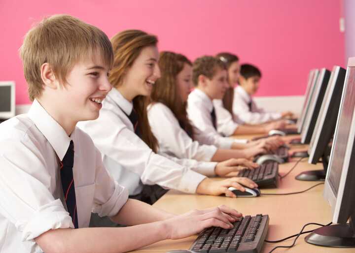 Students working on computers in a classroom with a pink wall.