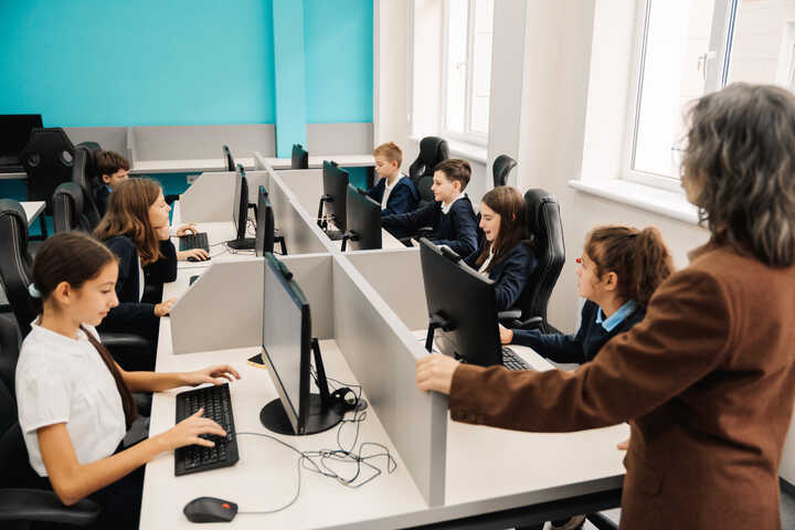 A classroom with students at computers and a teacher observing them.