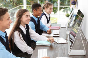 Four students at computers, engaged and smiling, in a bright learning environment.