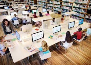 A library with students using computers at study desks and bookshelves in the background.