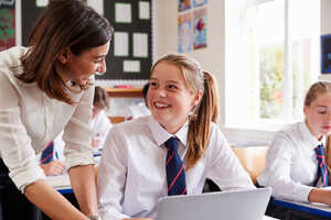 Teacher assisting a smiling student at a laptop in a classroom setting.