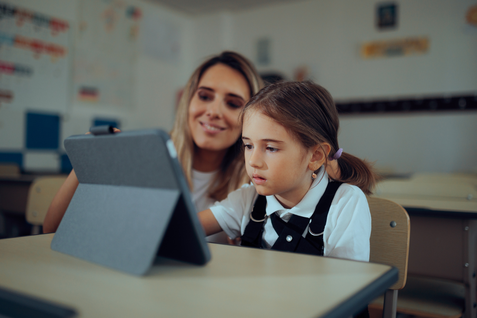A child and adult are focused on a tablet in a classroom setting.
