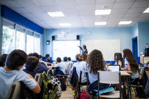 A classroom scene with students watching a teacher present at the front.