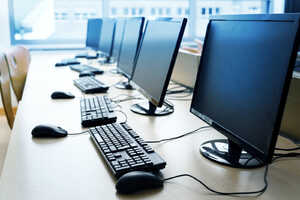 Five computer monitors with keyboards and mice arranged on a table in an office setting.