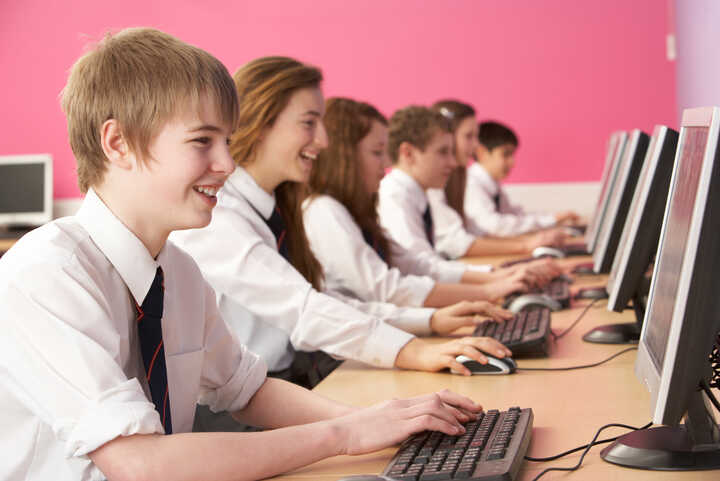 Students working on computers in a classroom with a pink wall background.