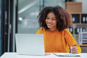 Smiling woman with curly hair working on a laptop at a desk.