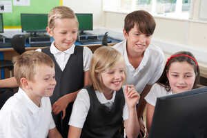Five children in school uniforms gathered around a computer, smiling and engaged.