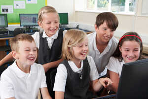 Five smiling children gather around a computer, looking at the screen in excitement.