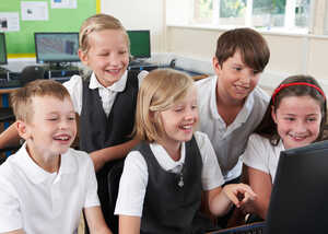 Five smiling children gathered around a computer, engaging with a screen.
