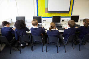 Children sitting at computers in a classroom, viewed from the back.