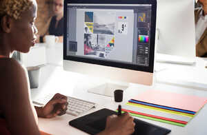 A person using a digital tablet and computer for design work at a desk.