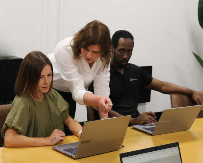 Three people in an office collaborate at laptops during a meeting.
