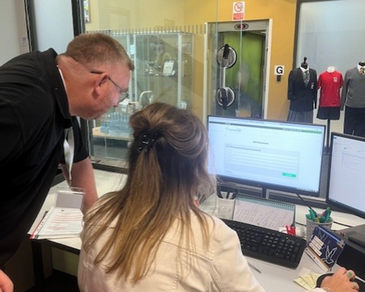 A Computeam IT professional assists a staff member of Pope Francis MAT with Learning Locker at a computer desk