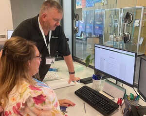 A Computeam IT professional assists a staff member of Pope Francis MAT with Learning Locker at a computer desk