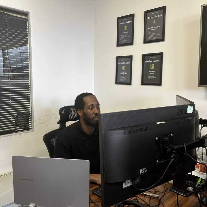 Computeam 1st line apprentice working at a desk with multiple monitors in a modern office setting.