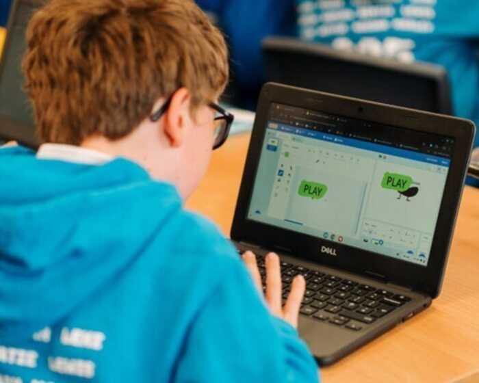 A child in a blue hoodie using a laptop, working on a project with "PLAY" displayed on screen.