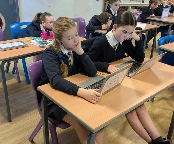 Students working on laptops in a classroom with colorful chairs.
