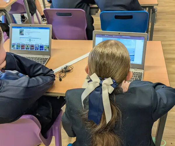 Three students in a classroom collaborate at laptops during a lesson