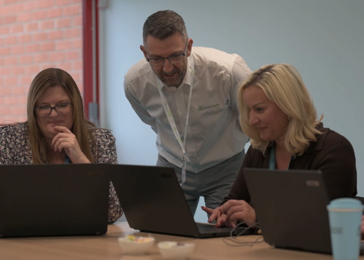 A young boy with headphones smiles while using a computer in a classroom setting.