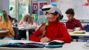 A student wearing a VR headset sits at a classroom desk while others work nearby.